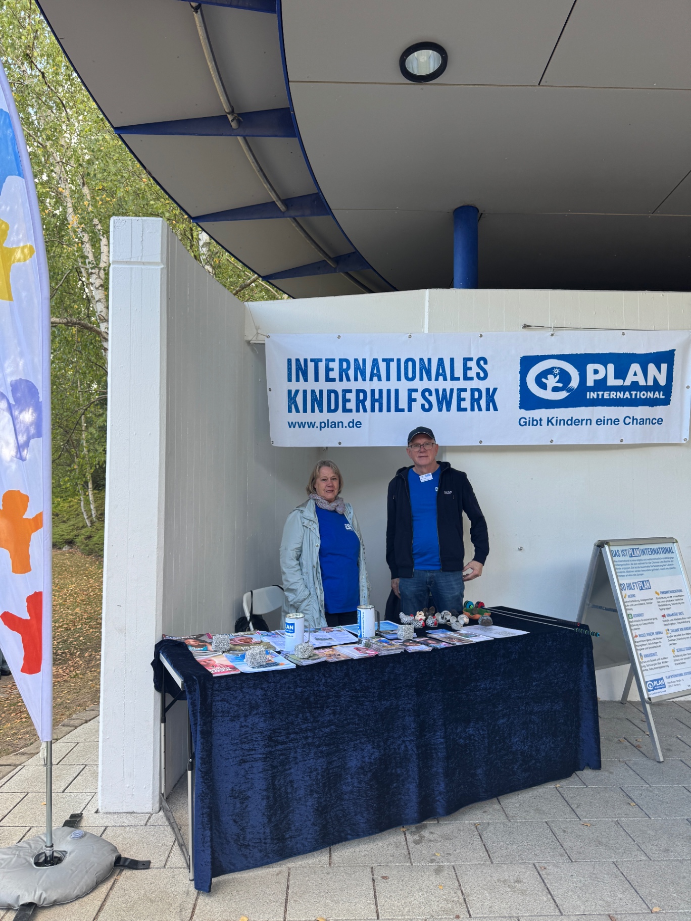 Stand von Plan International mit Infomaterial und zwei Helferinnen