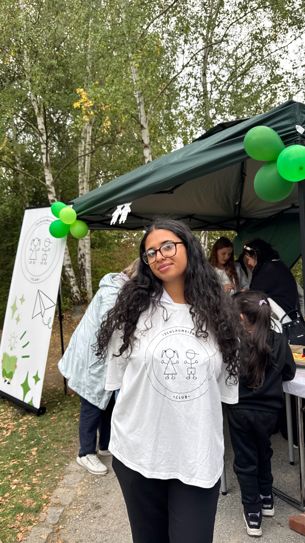 Teammitglied im Schlaumeierclub-Shirt vor dem Festzelt mit grünen Ballons