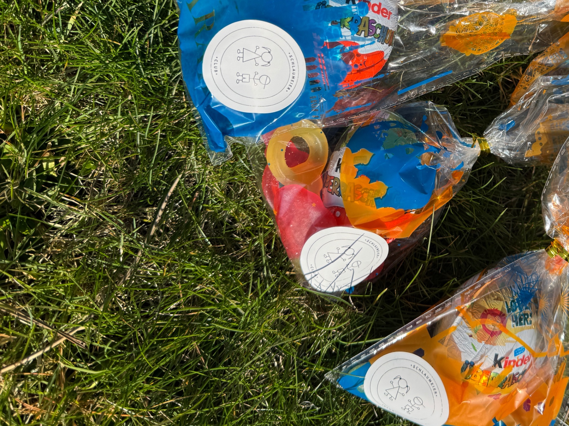 Kinder halten bunte Schlaumeierclub-Tüten mit Ostereiern und Süßigkeiten in die Kamera